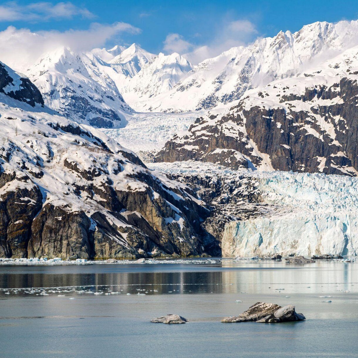Snow-covered mountains and a massive tidewater glacier meeting calm water in Glacier Bay National Park.