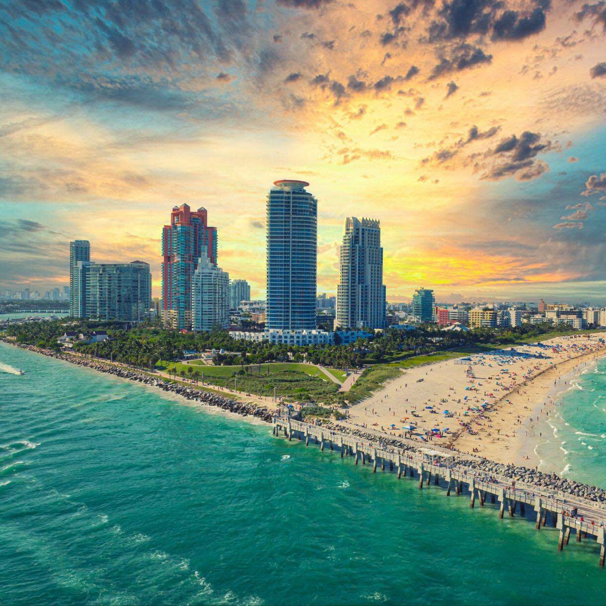 Aerial view of Miami Beach, Florida at sunset, showcasing tall buildings along the coast, sandy beaches and the turquoise waters of the Atlantic Ocean.
