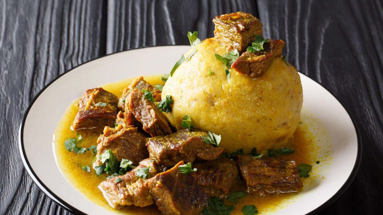 Plate of Puerto Rican mofongo made with mashed plantains and topped with tender stewed beef chunks in a golden garlic sauce.