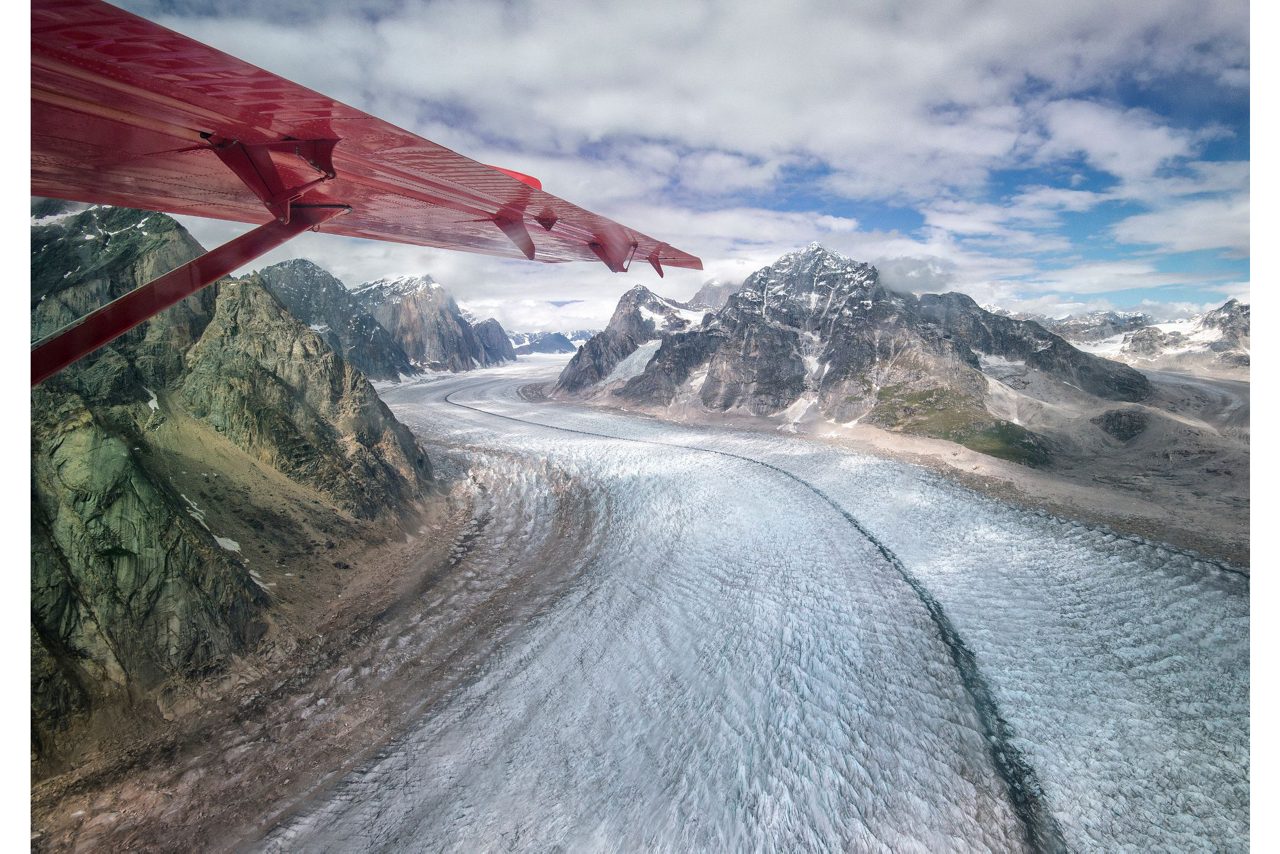 Aerial view of a vast glacier winding between rugged, snow-capped mountains.