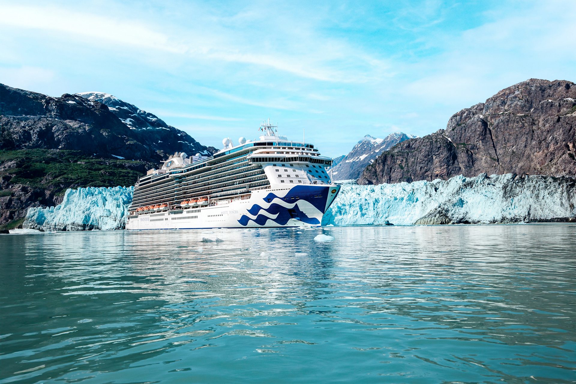 A cruise ship sails near a glacier with mountainous scenery.