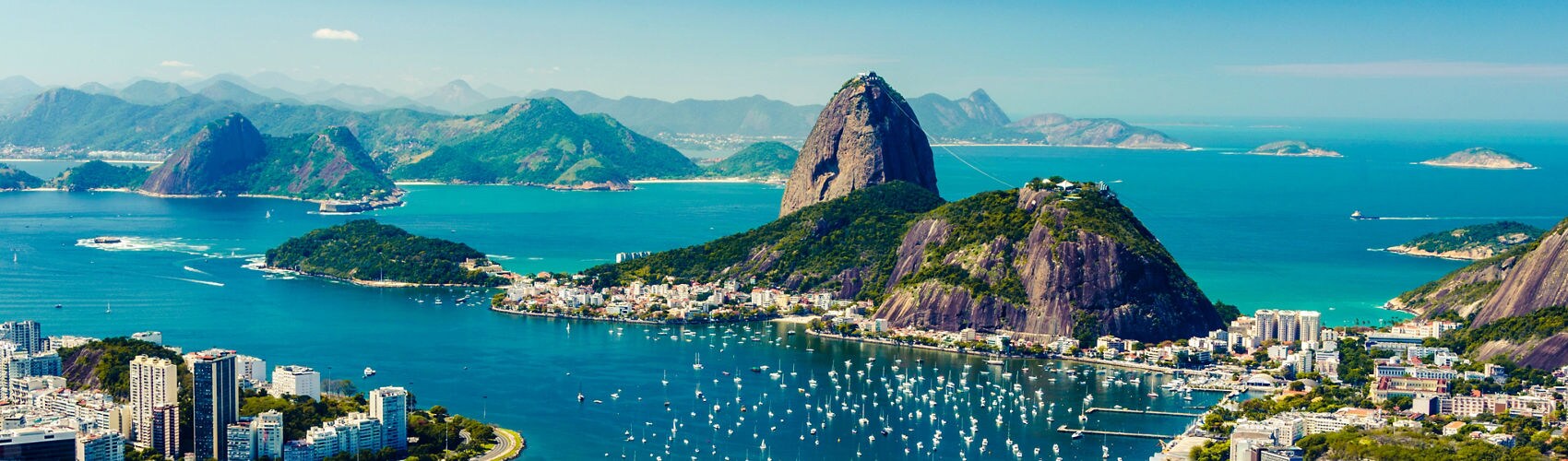 Aerial view of Rio de Janeiro's Sugarloaf Mountain rising above a turquoise bay with the city skyline in the background