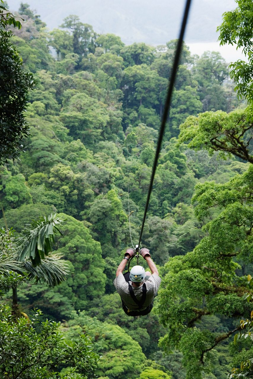 person in protective gear, ziplining above the treeline