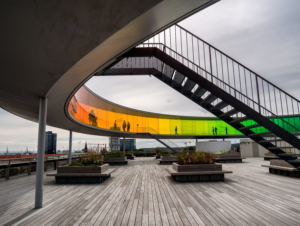 Circular rainbow-colored glass walkway on the rooftop of ARoS Aarhus Art Museum with silhouettes of visitors.