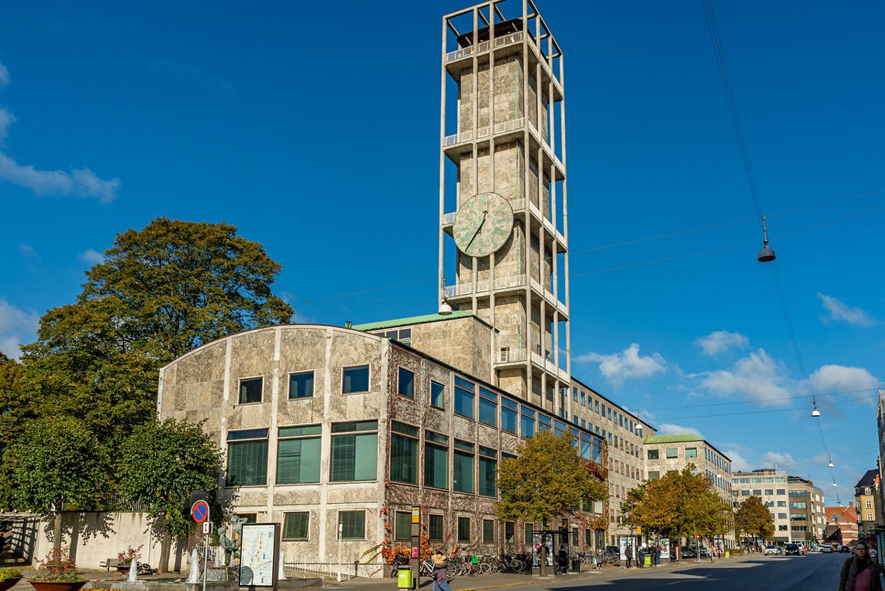Aarhus Town Hall in Denmark with tall stone clock tower and rectangular windows under a clear blue sky.