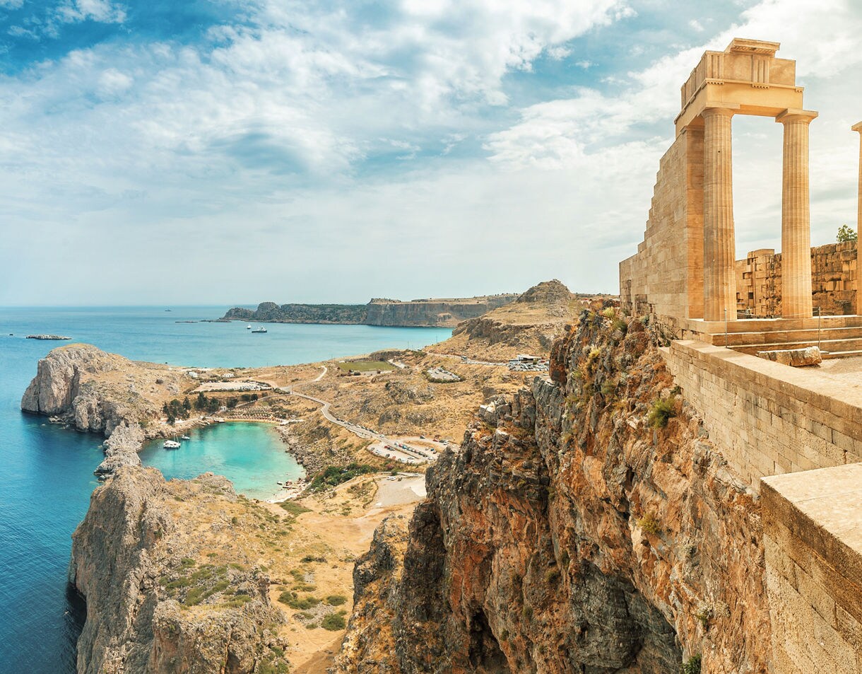 Ancient stone columns of the Acropolis of Lindos perched on a cliff above turquoise waters and rugged coastline on the island of Rhodes, Greece.