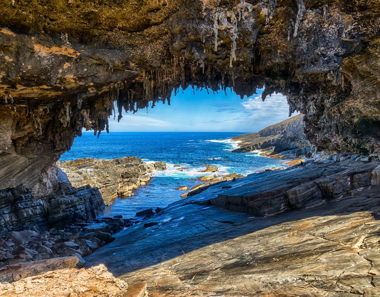 Natural rock arch framing a view of blue ocean and jagged coastal cliffs under bright daylight.