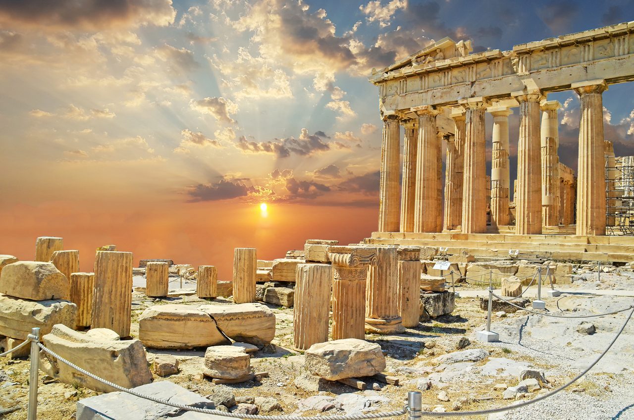 Sun rays break through golden clouds behind the columns of the Parthenon, with fallen marble blocks and rope barriers in the foreground.