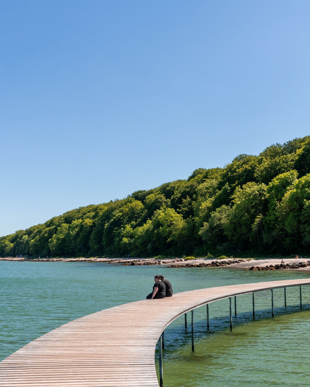 Wooden circular pier known as the Infinite Bridge extending over green water with forested coastline in Aarhus.