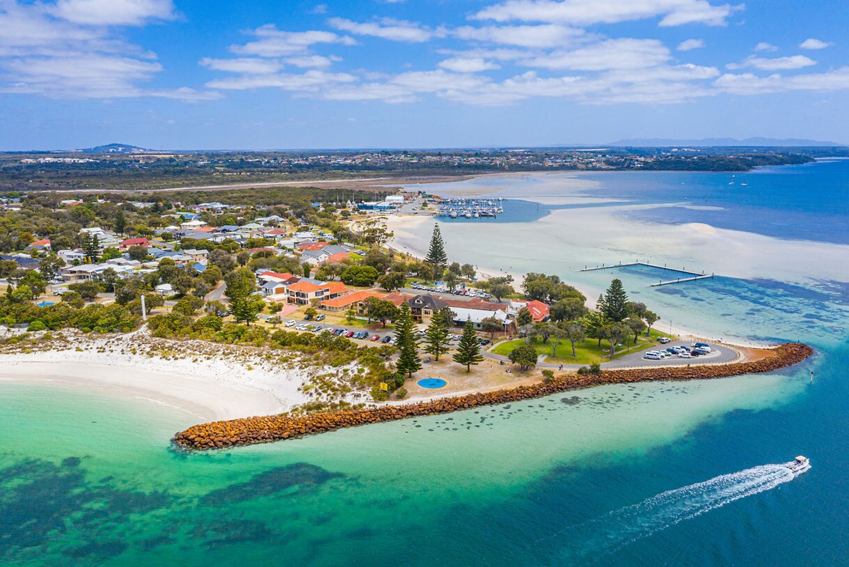 Aerial view of a coastal town with white sand beaches, shallow turquoise water and boats offshore.