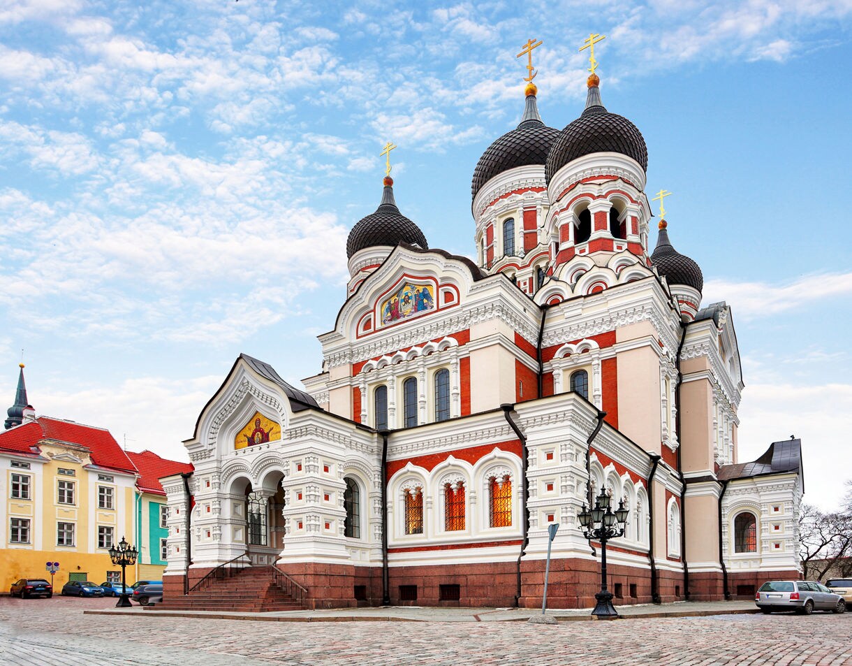 Alexander Nevsky Cathedral in Tallinn, Estonia, a Russian Orthodox church with ornate red-and-white façades, black onion domes and golden crosses set against a blue sky.