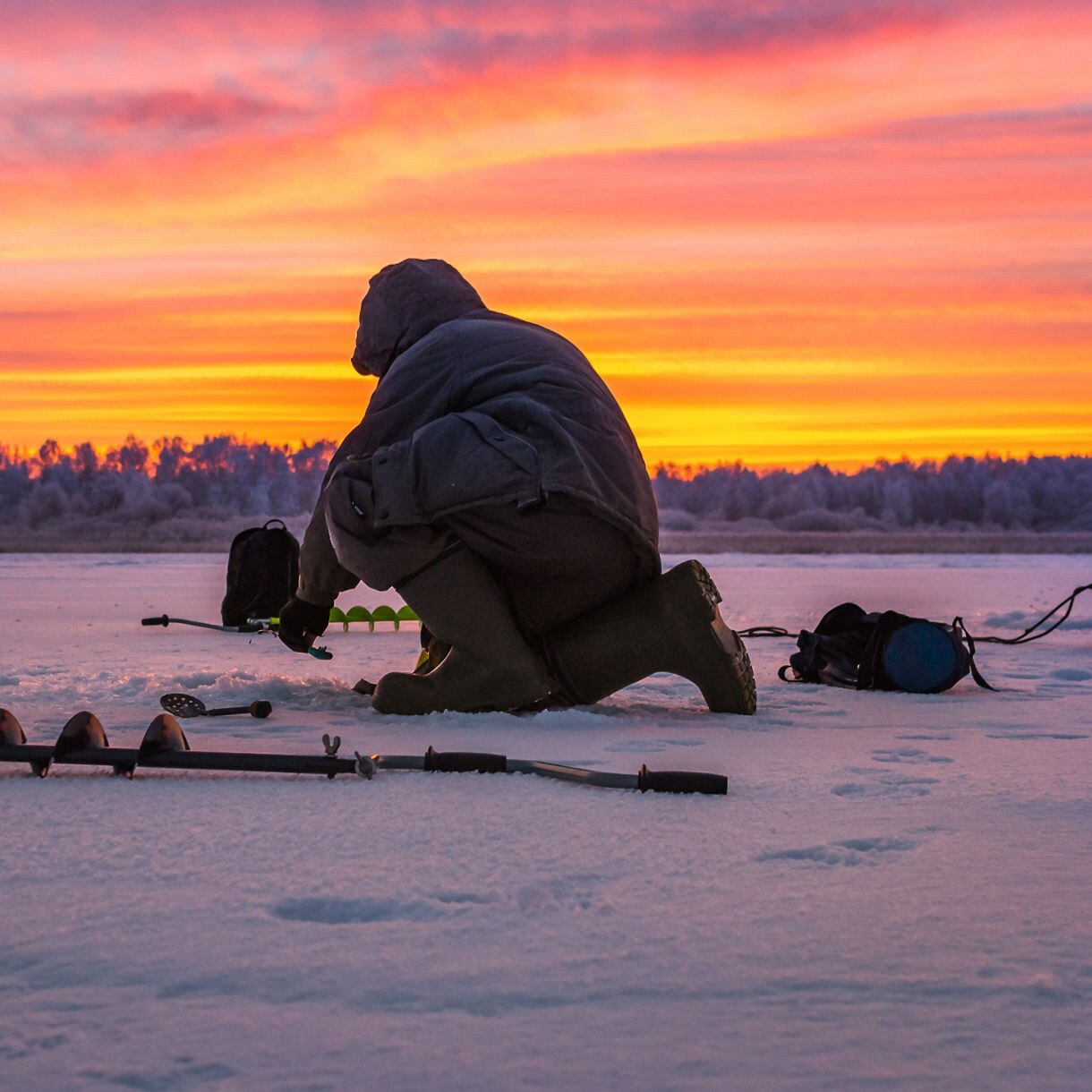 Person dressed in winter gear ice fishing at sunset on a frozen lake in Alta, Norway.
