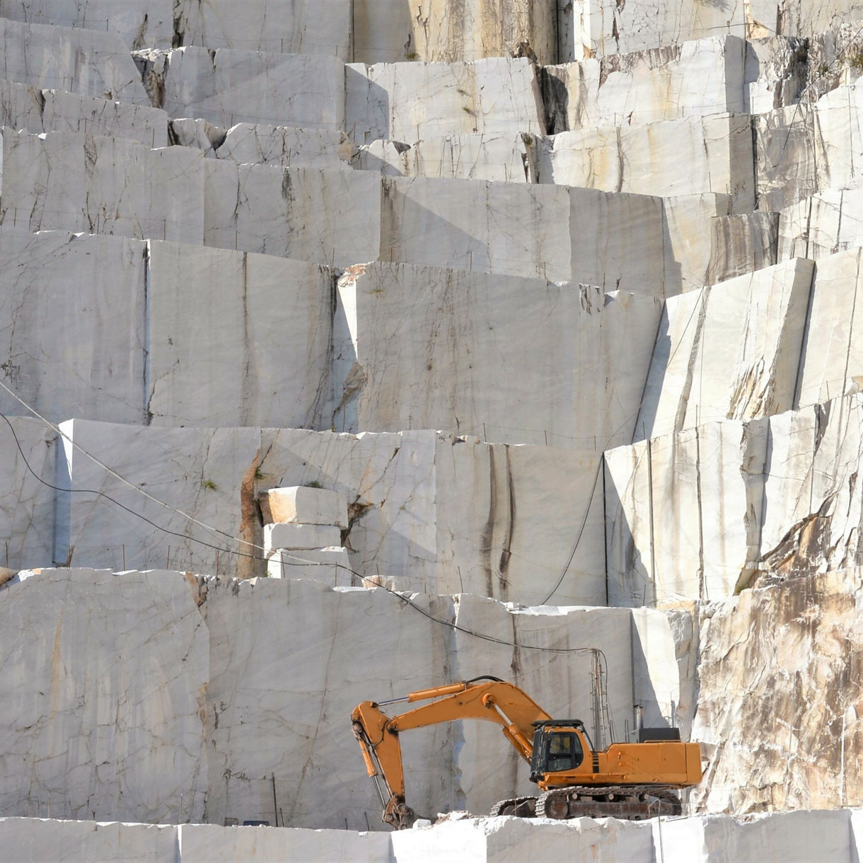 Excavator working at a marble quarry in Alta, Norway, surrounded by massive vertical slabs of stone.