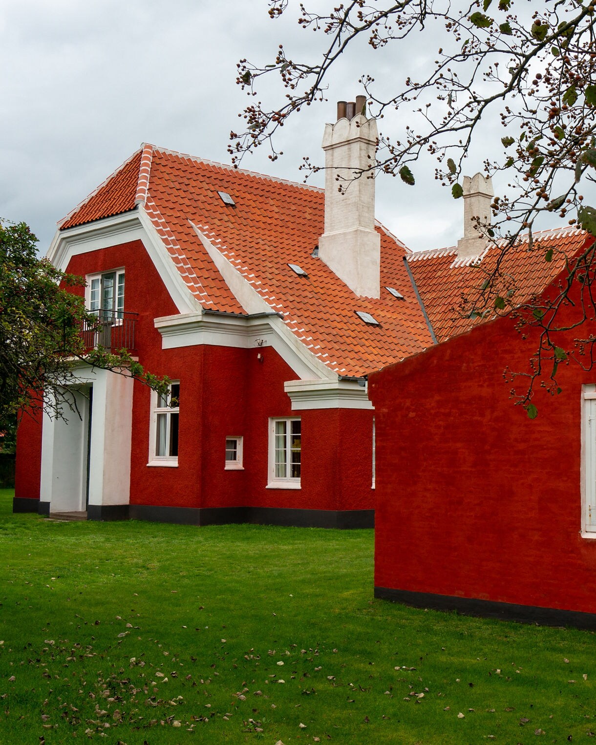 Red-brick house with orange roof tiles and white-trimmed windows, surrounded by green grass at Anchers Hus in Skagen.