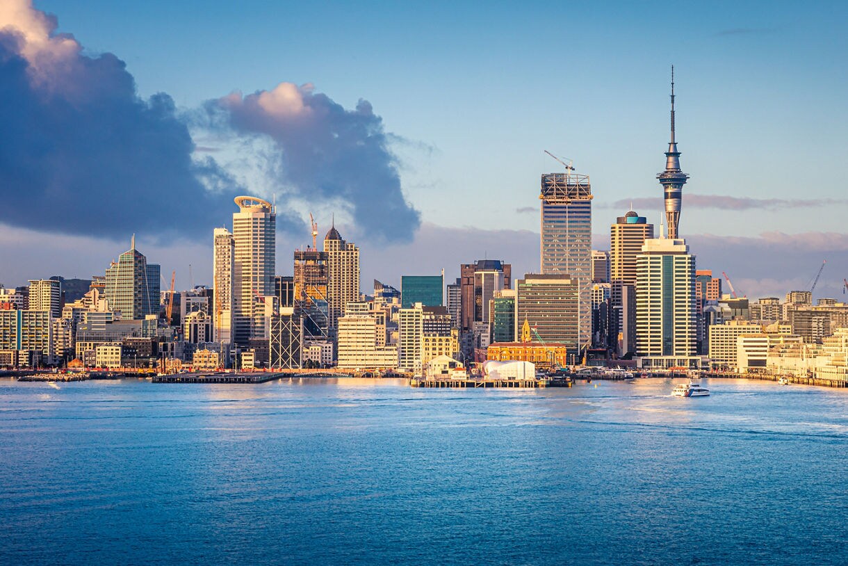 Panoramic view of Auckland’s waterfront with modern skyscrapers, the Sky Tower and boats on the harbor.