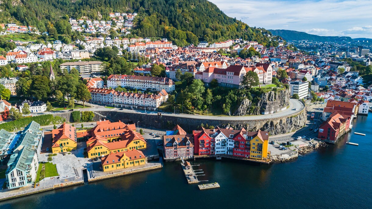 Aerial view of Bergen with colorful houses by the harbor, winding roads and forested mountainside.