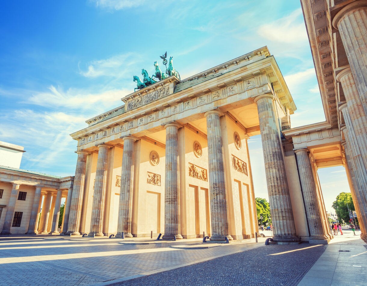 Brandenburg Gate in Berlin with tall sandstone columns, detailed carvings and the bronze quadriga statue on top under a bright blue sky.