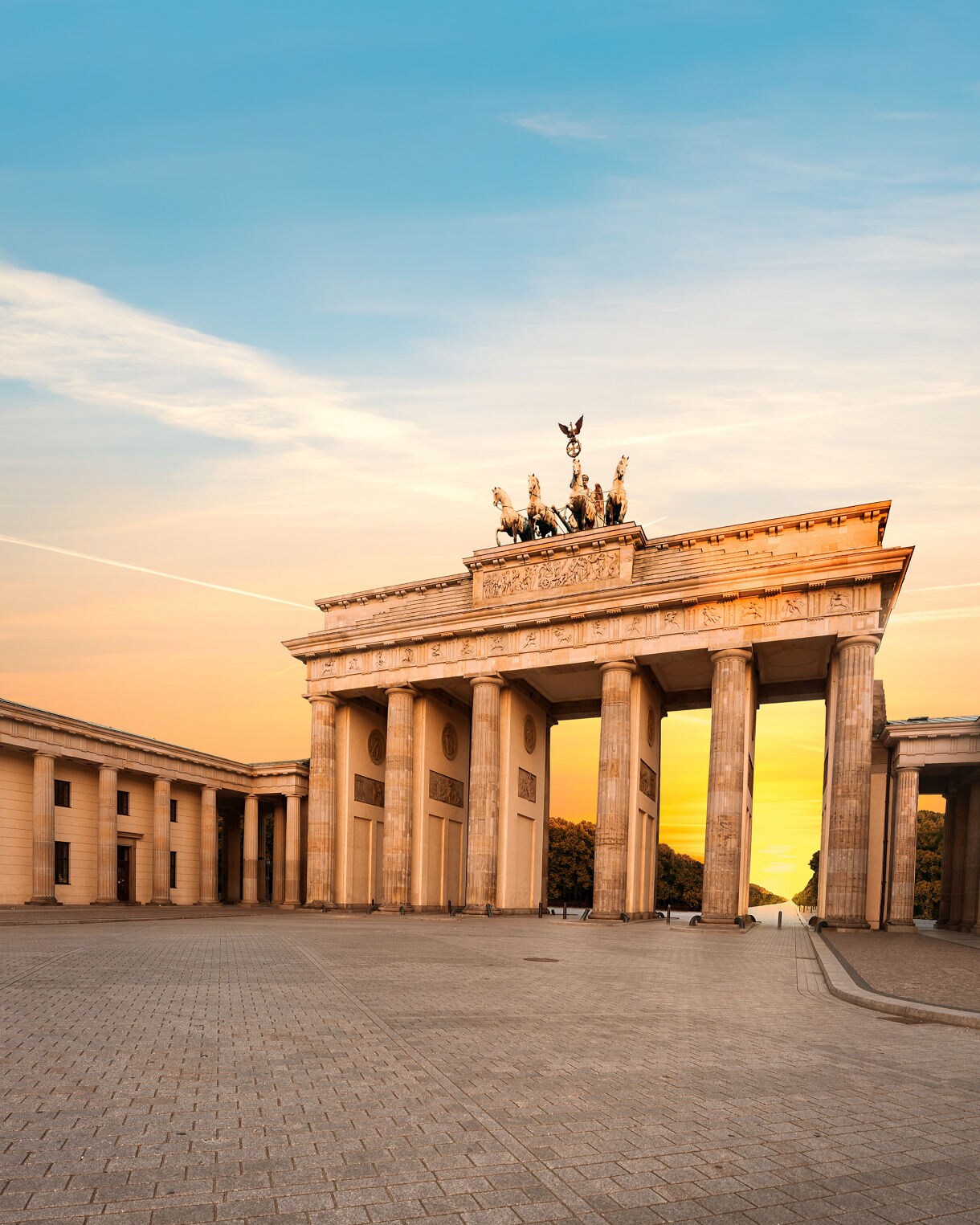 The Brandenburg Gate in Berlin at sunset with golden light illuminating its neoclassical columns and quadriga statue against a pastel sky.