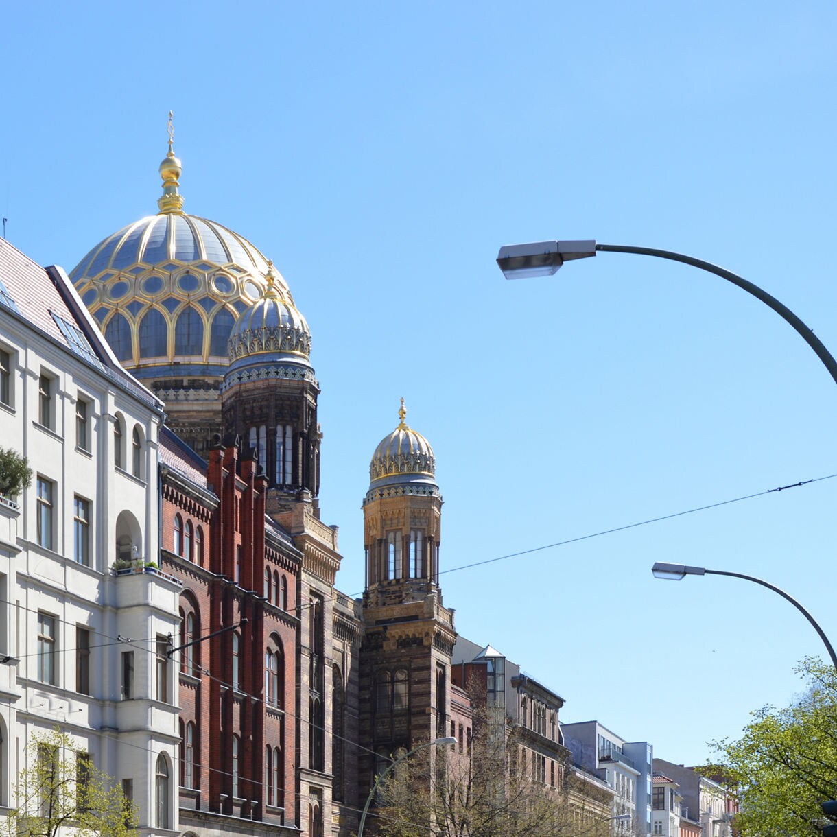 View of Berlin’s New Synagogue with its ornate golden dome and towers rising above surrounding residential buildings on a clear day.