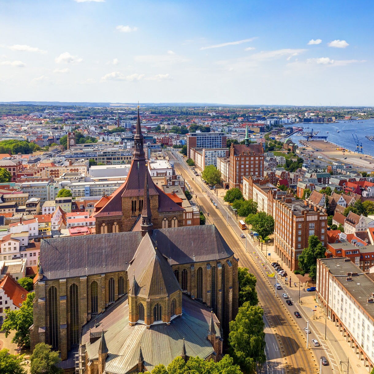 Aerial view of Rostock, Germany with St. Mary’s Church in the foreground, rows of colorful houses and a harbor filled with ships and sailboats along the river.