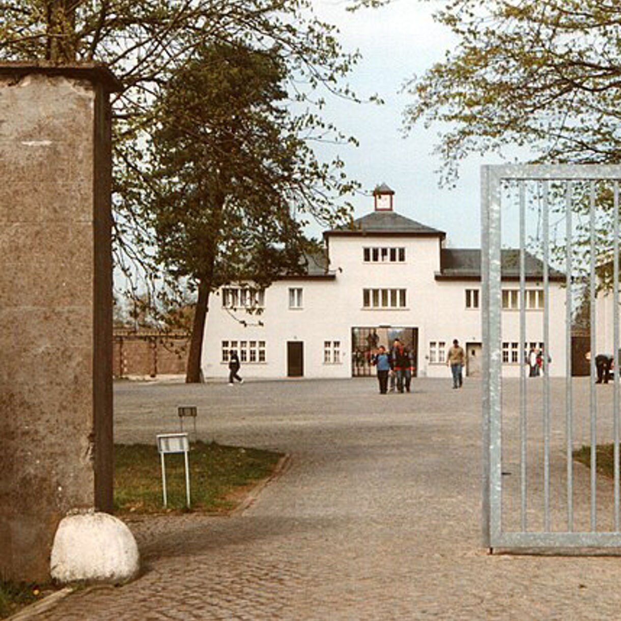 View through the gates of Sachsenhausen concentration camp memorial in Germany showing the entrance building with visitors walking across the courtyard.