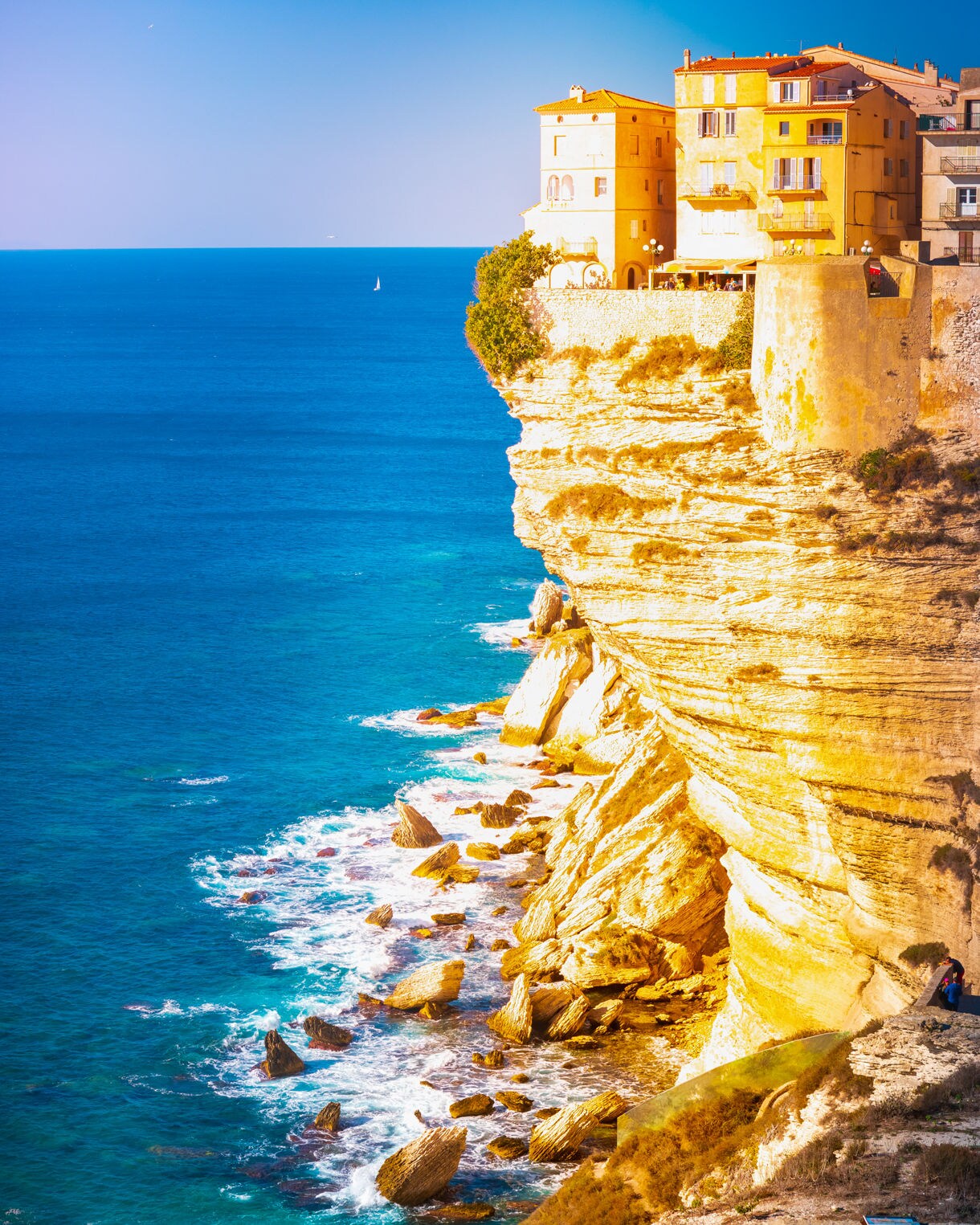 Colorful buildings of Bonifacio’s citadel in Corsica standing on steep white cliffs above turquoise Mediterranean waters.