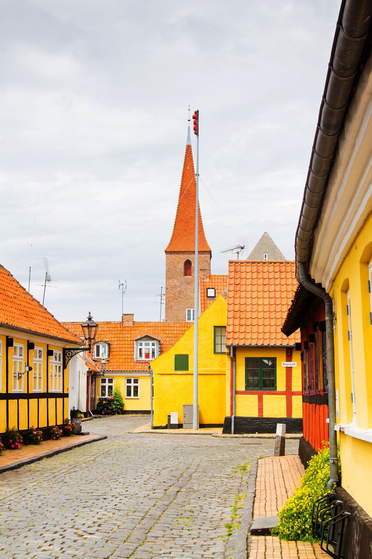 Colorful historic houses in Rønne, Bornholm with yellow and red facades, orange tile roofs, cobblestone streets and a tall brick church spire rising in the background.
