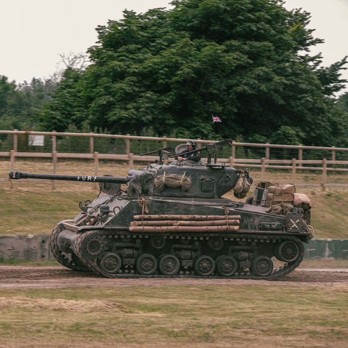 World War II Sherman tank nicknamed "Fury" on display at Bovington Tank Museum, driving along a dirt track with a Union Jack flag and a crew member visible on top.