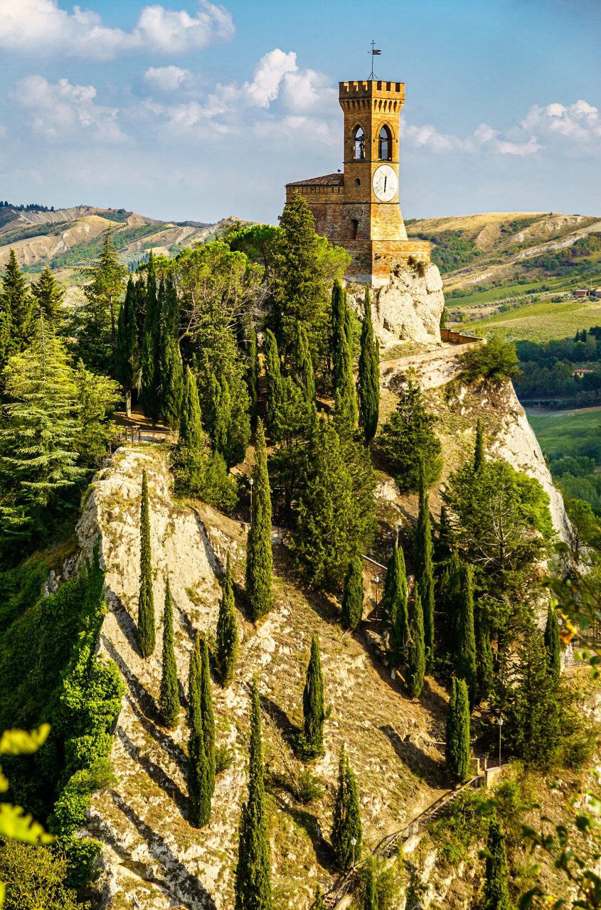 Clock tower atop a rocky hill in Brisighella overlooking cypress trees and the rolling countryside of Emilia-Romagna.