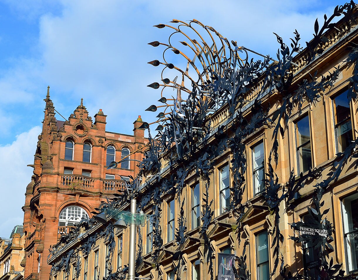 Decorative metalwork covering the façade of a building on Buchanan Street in Glasgow, with a red sandstone tower in the background.