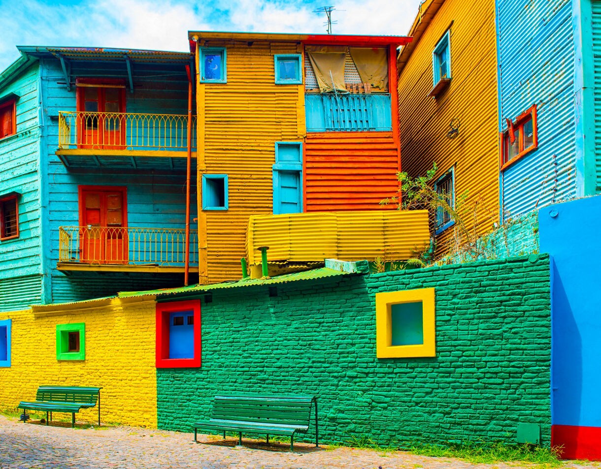 Brightly painted buildings in blue, yellow, green and red line a cobblestone street with simple benches.
