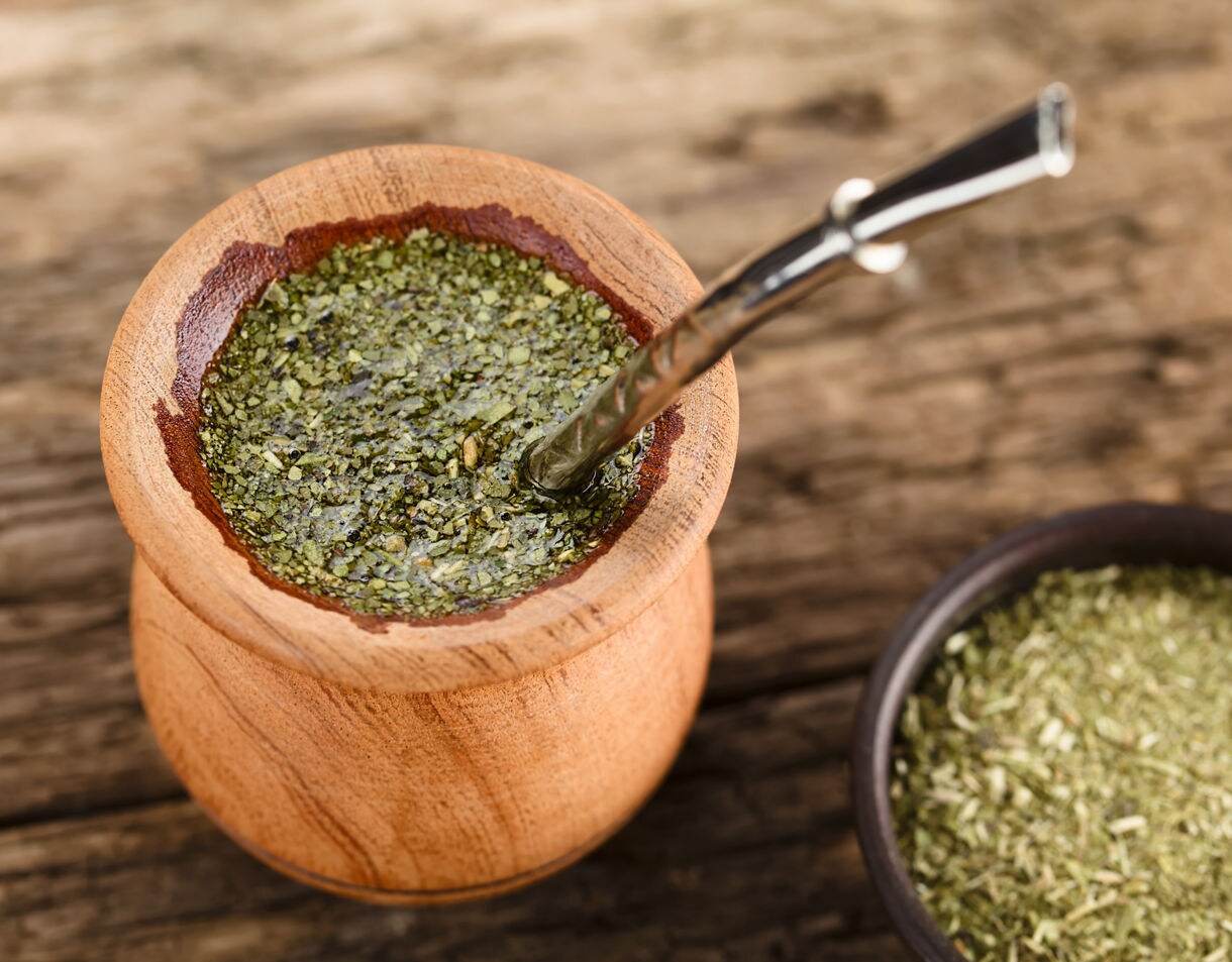 Close-up of a wooden mate gourd filled with yerba and a metal straw on a rustic table.