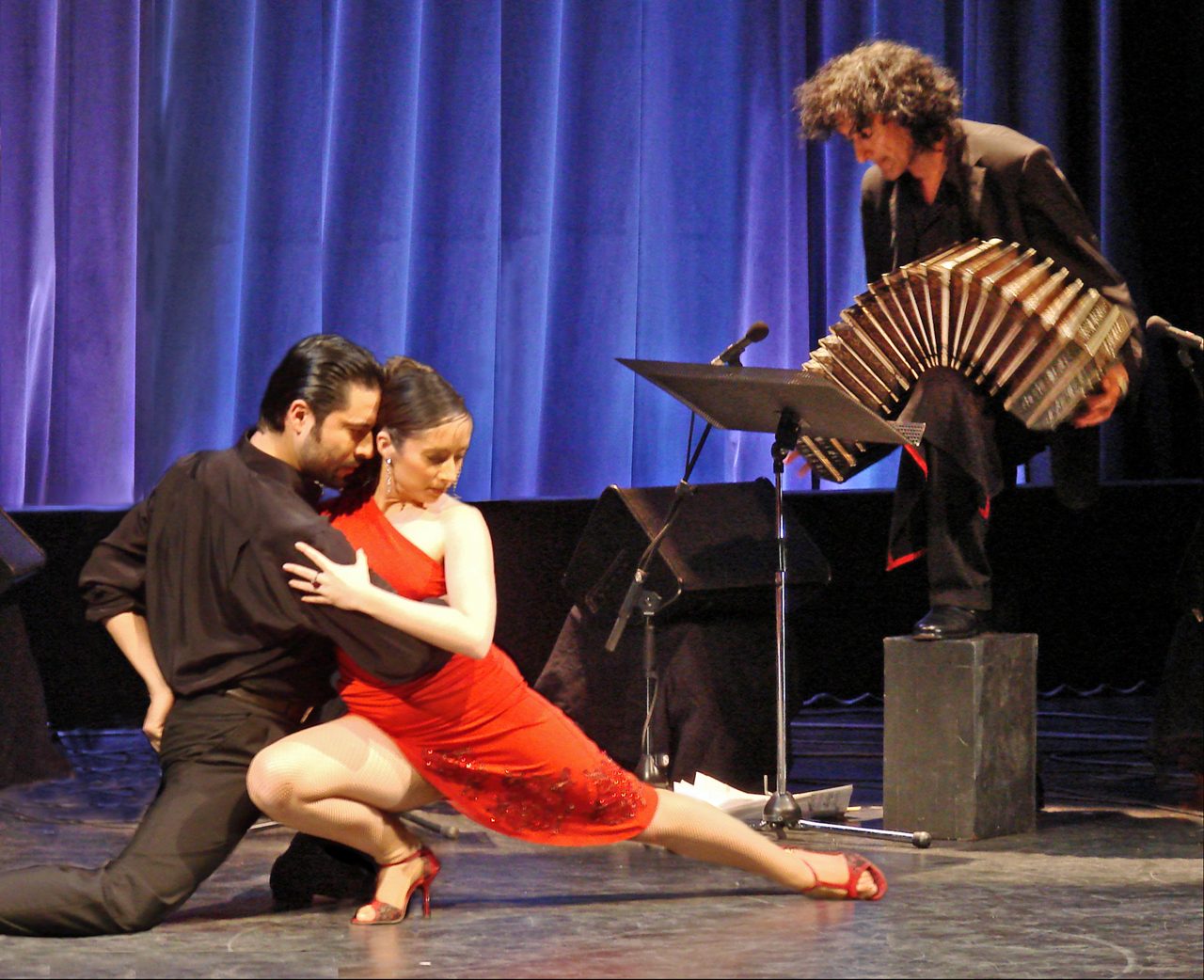 Tango couple in formal attire, woman in a flowing red dress mid-turn on the dance floor.