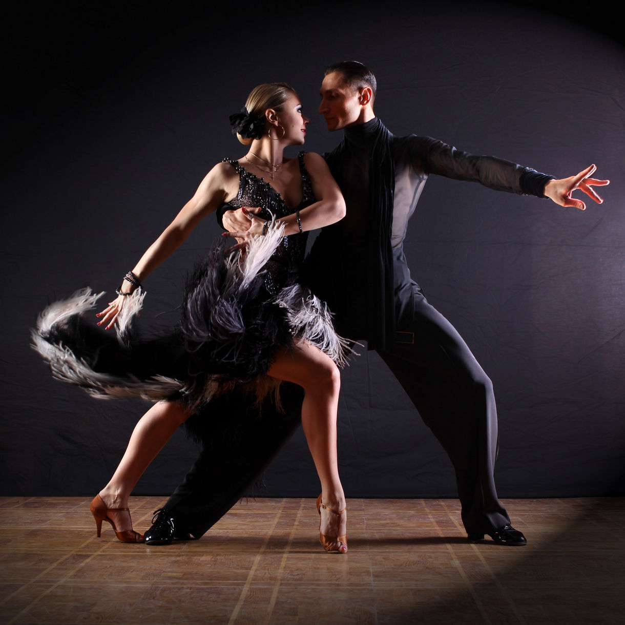 Tango couple in dramatic pose, spotlight highlighting their intense connection and flowing black dress.