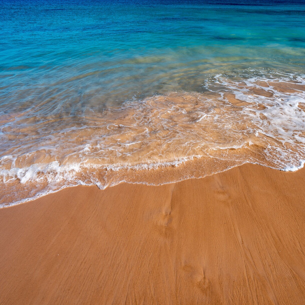 Turquoise waves gently washing over smooth golden sand on a sunny beach.