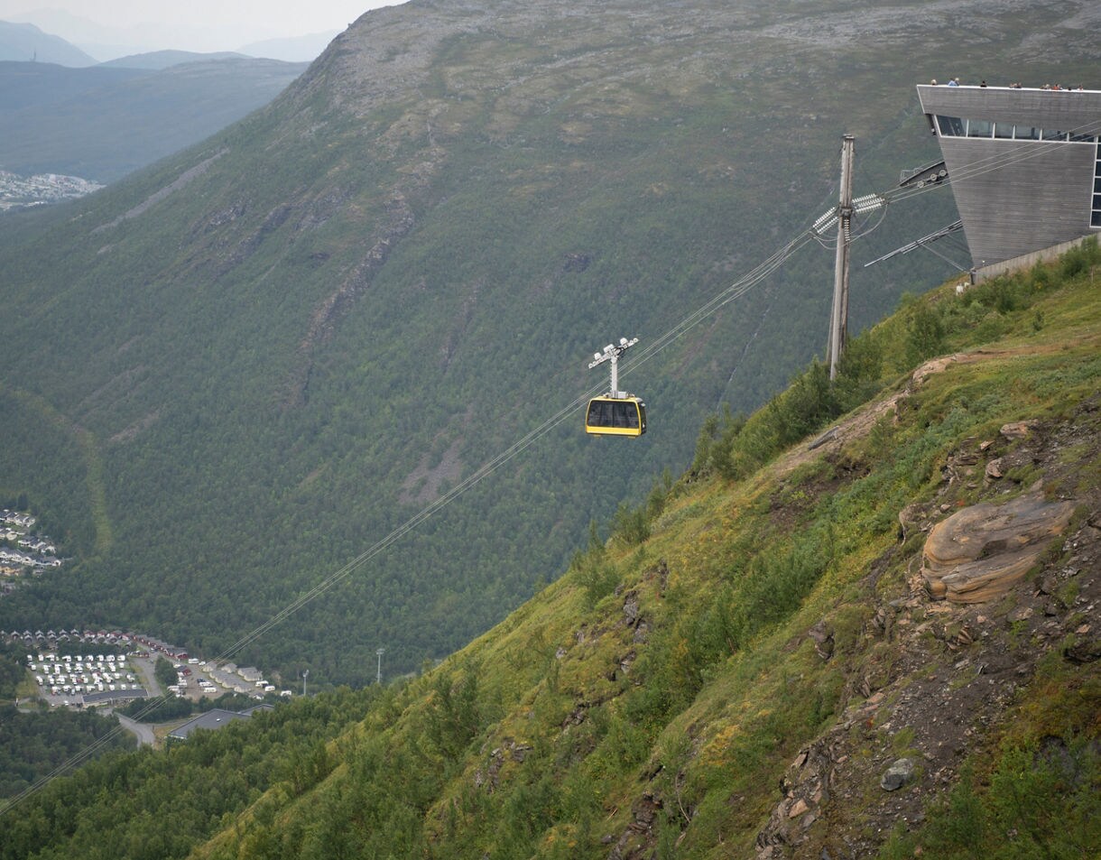 Yellow cable car traveling up a steep green mountainside near Tromsø, with panoramic views of the valley and town below.