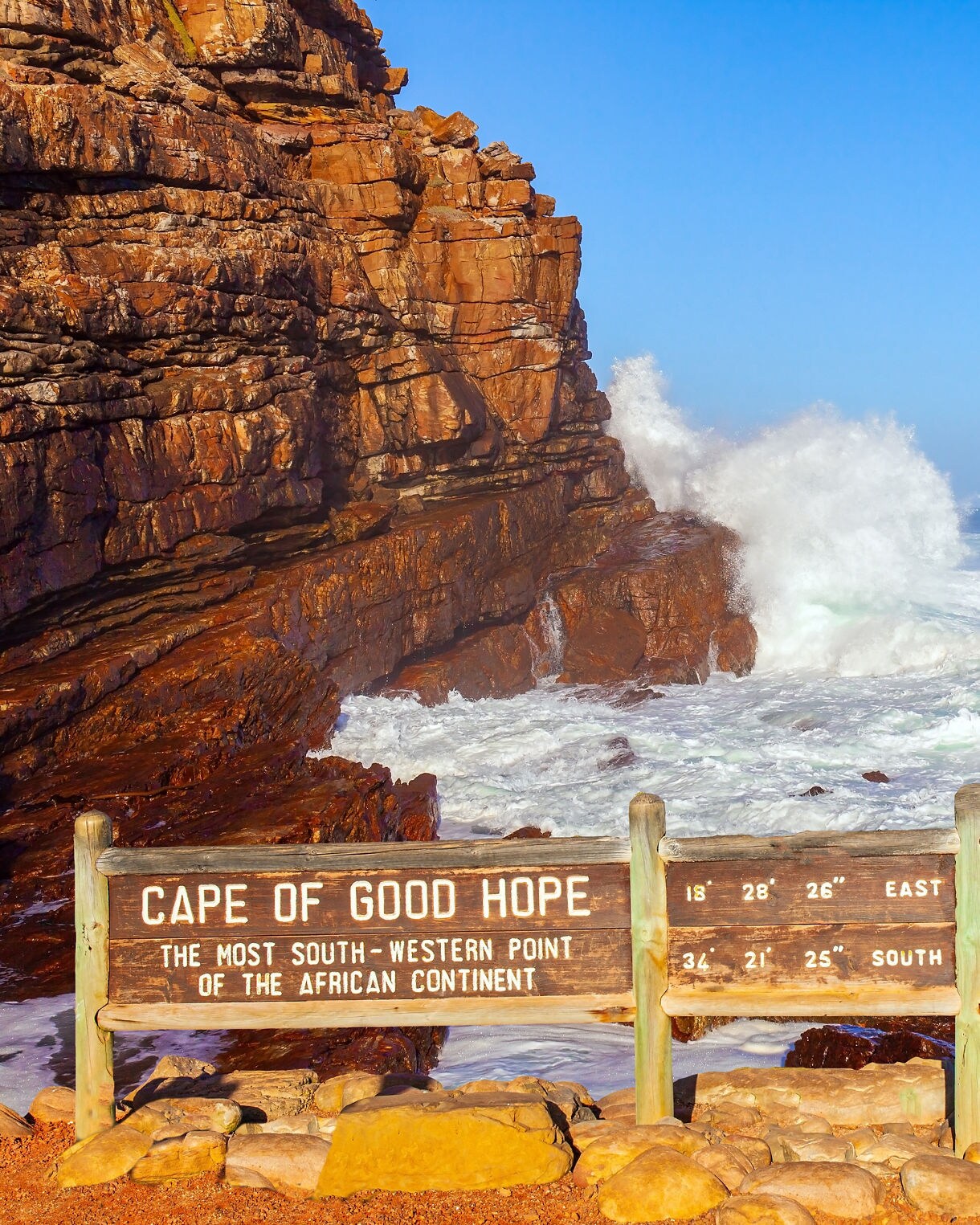 Sign at the Cape of Good Hope in front of rocky cliffs and strong ocean waves
