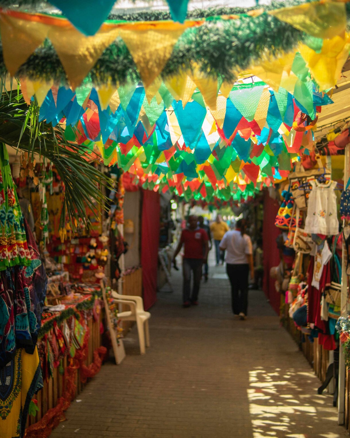 Colorful market in Cartagena, Colombia with hanging banners, handmade clothing, crafts and shoppers walking through narrow stalls.