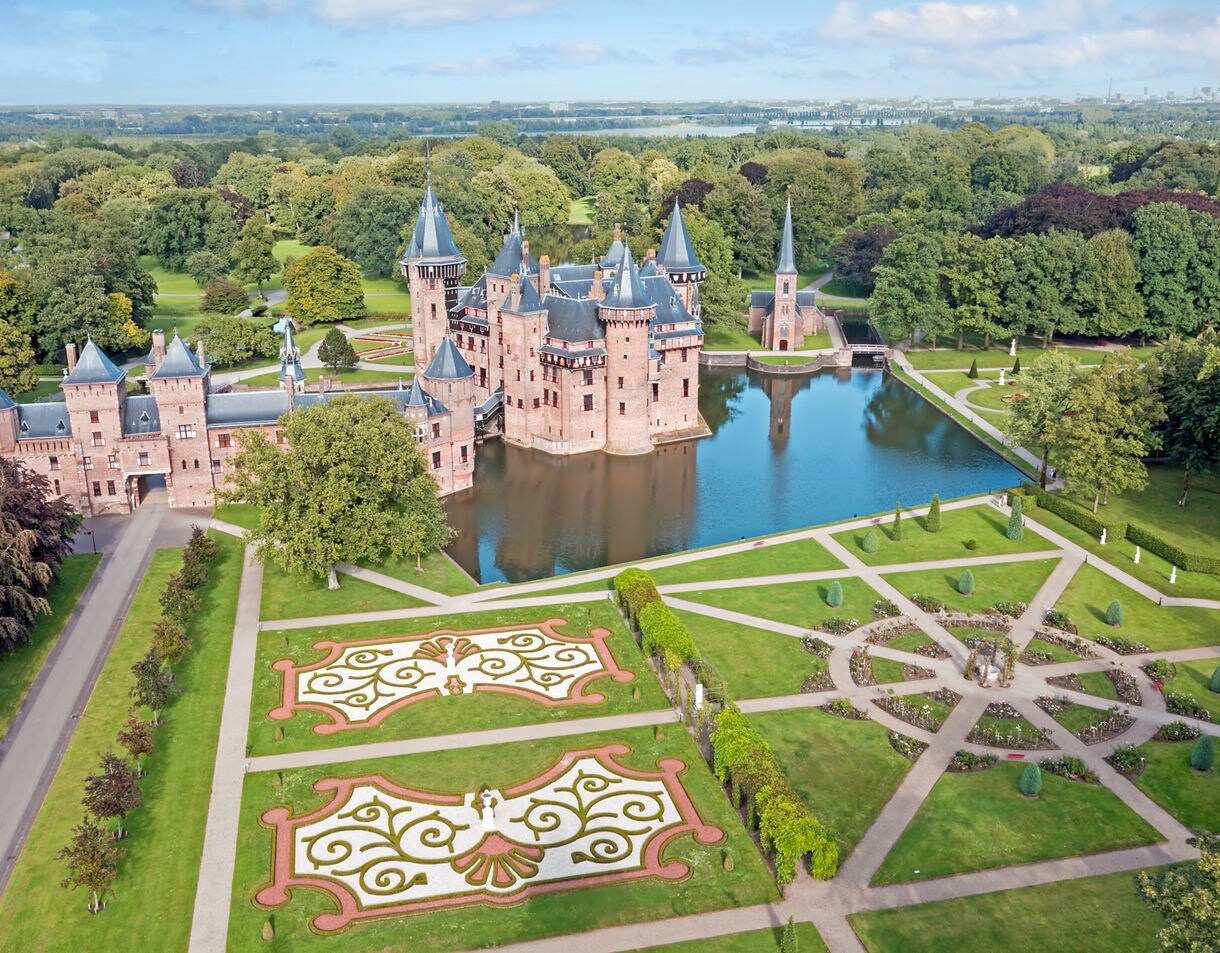 Aerial view of Castle De Haar in the Netherlands showing its brick towers, reflective moat and sprawling geometric gardens surrounded by lush green parkland.