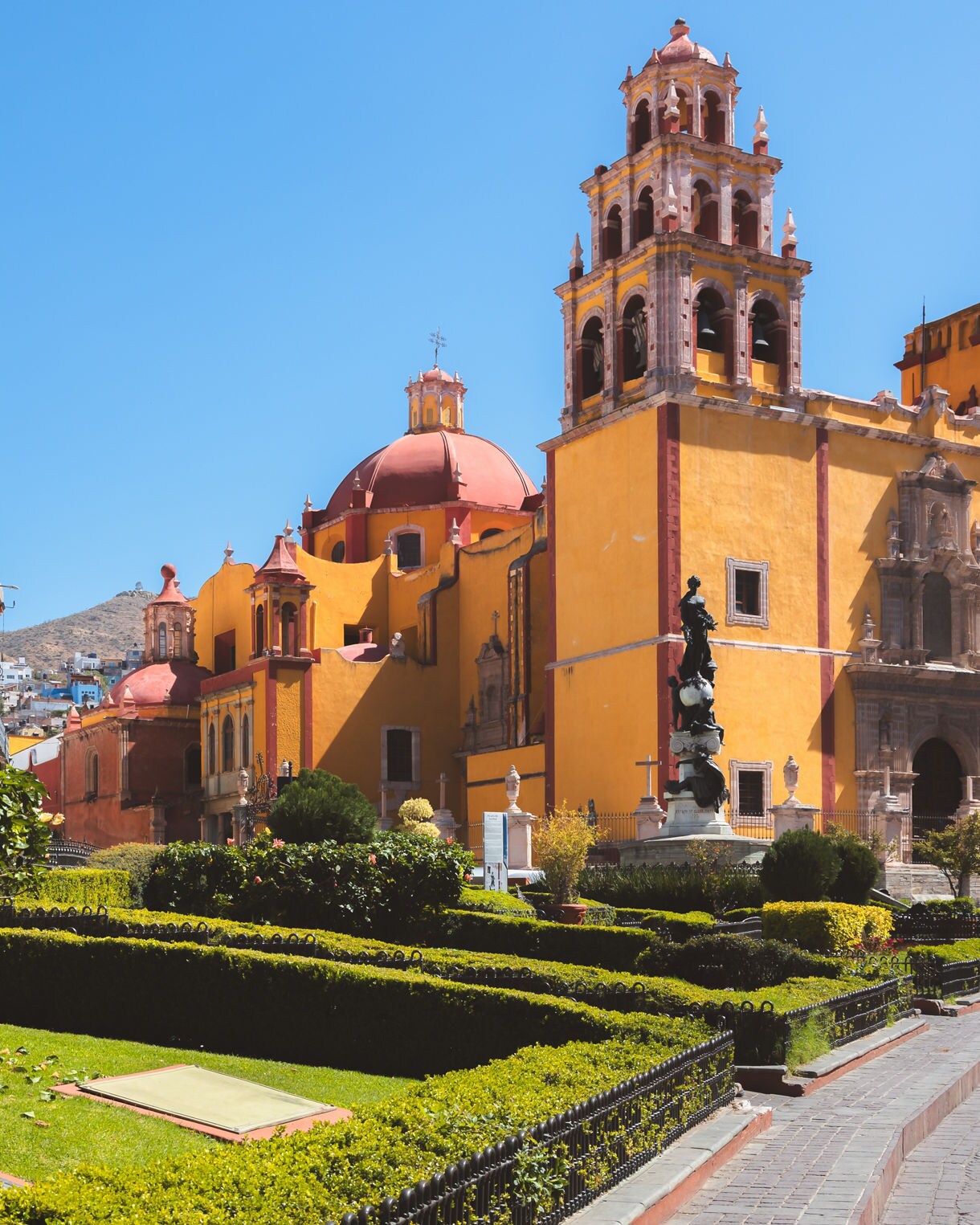 Basílica de Nuestra Señora de Guanajuato with its bright yellow walls, red domes and bell towers framed by a manicured garden.