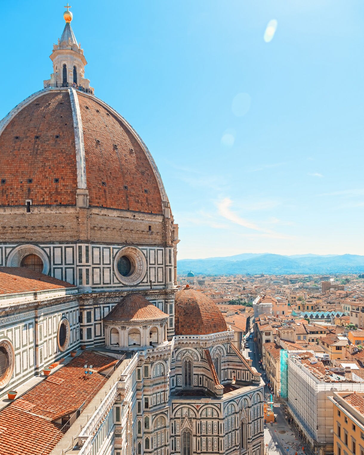 A close view of the red-tiled dome of Florence’s Cathedral of Santa Maria del Fiore, with intricate marble patterns on the walls and the city stretching out below under a clear blue sky.
