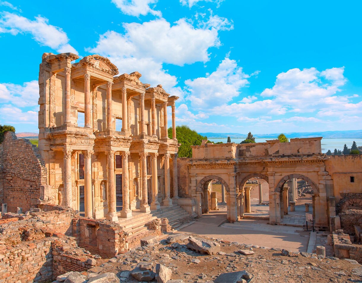 Ruins of the Library of Celsus in Ephesus with tall marble columns, carved details and surrounding stone walls under a bright blue sky.