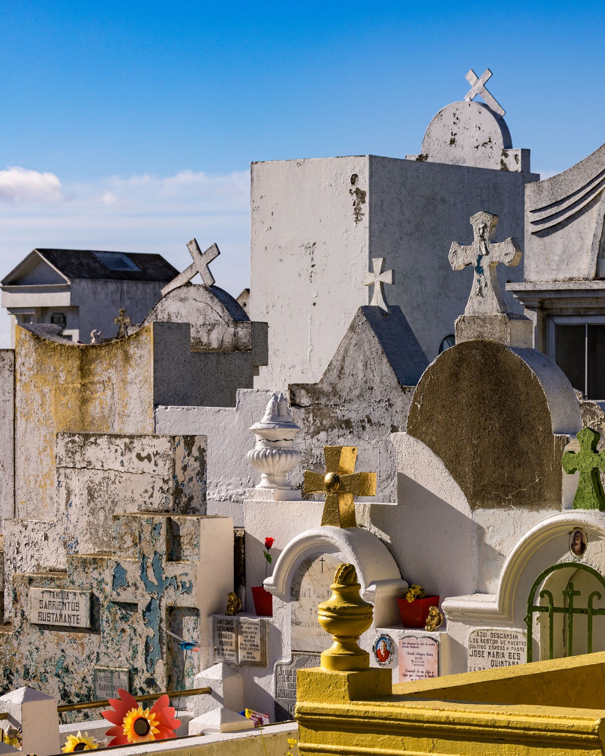 Colorful above-ground tombs and weathered crosses in Punta Arenas’ municipal cemetery, with white and yellow mausoleums clustered under a clear blue sky.