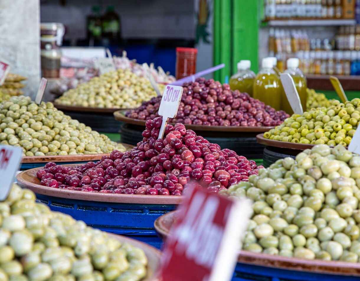 Heaped trays of green and red olives displayed for sale in a busy market.