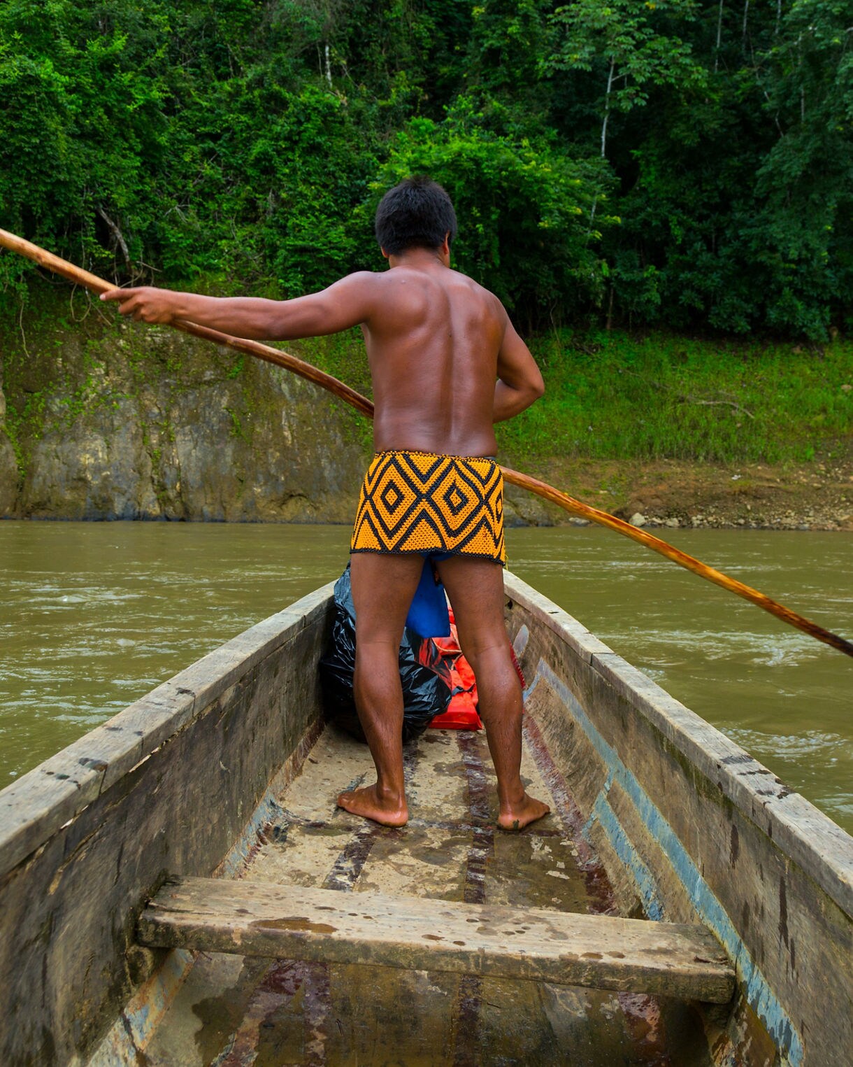 Emberá guide paddling a wooden canoe along the Chagres River in Panama, surrounded by dense green rainforest.