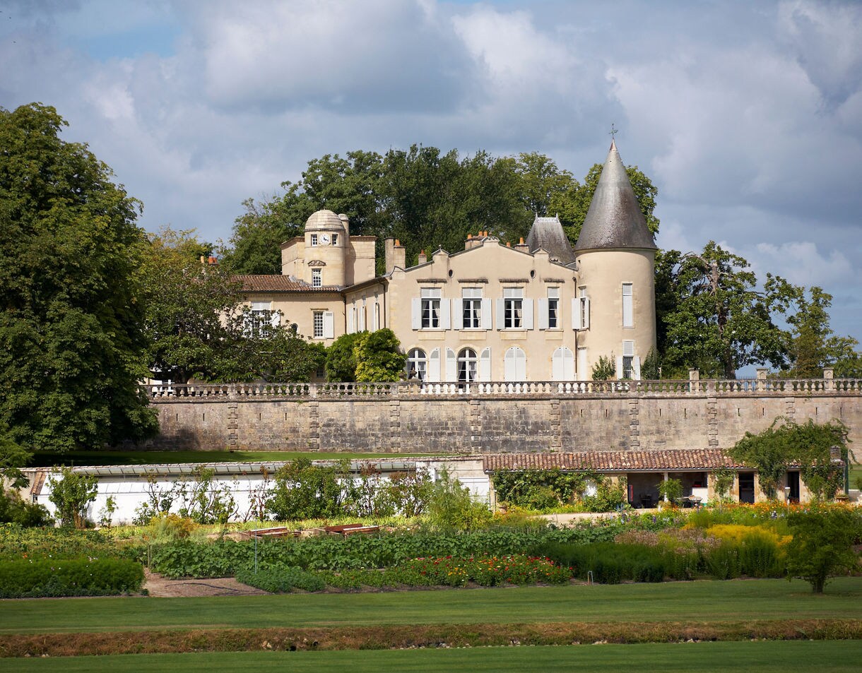 A grand, pale stone château with towers and shuttered windows set behind gardens and vineyards at Château Lafite Rothschild in Bordeaux.