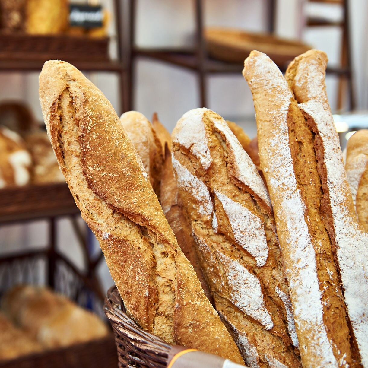 Close-up of golden baguettes in a basket with shelves of rustic loaves blurred in the background