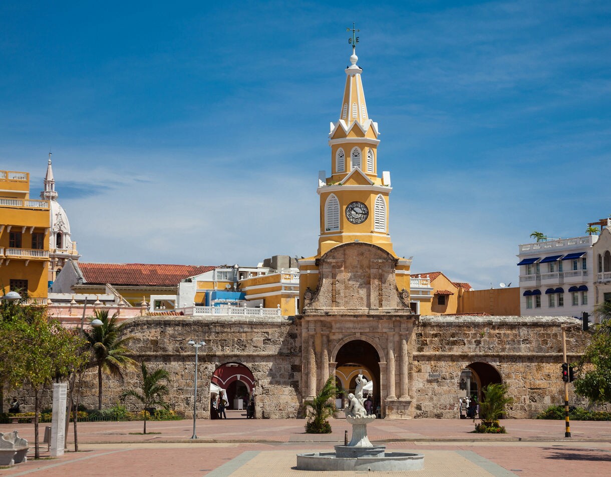 Yellow and white Clock Tower Gate in Cartagena, Colombia, rising above the old stone city wall with colonial buildings behind it.