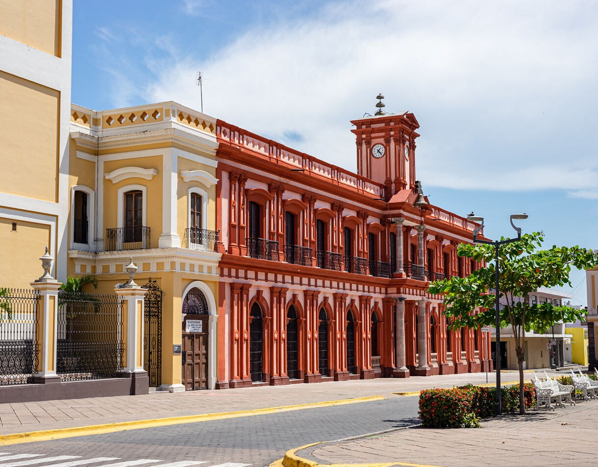 Colonial-style red and yellow buildings in downtown Colima with a clock tower, iron balconies and benches lining the street.