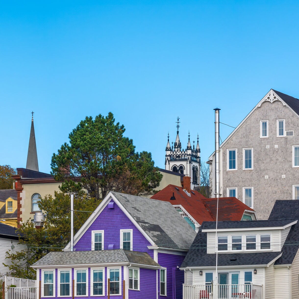 Row of colorful houses and historic buildings in Lunenburg, including purple, yellow and gray facades set against a clear blue sky.